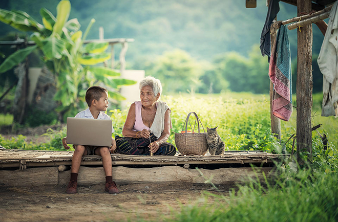 A little boy with a computer in his lap, sitting next to an old lady. They